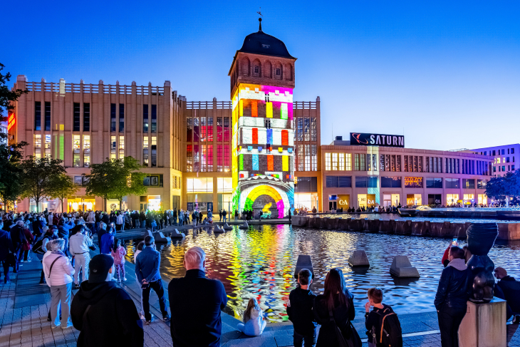Roter Turm in Chemnitz bei Nacht, beleuchtet mit bunten Lichtern, reflektiert im Wasserbecken